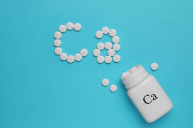 Açık mavi arkaplan üzerinde kalsiyum takviye hapları ile düz konum, metin için boşluk