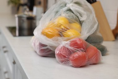 Mutfaktaki beyaz tezgahta farklı taze ürünlerin olduğu plastik torbalar.