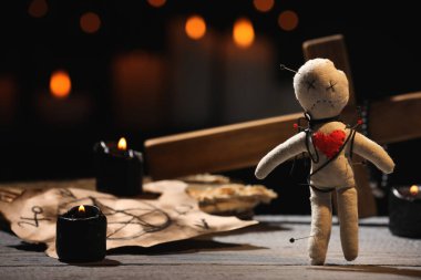 Voodoo bebeği, ahşap masanın üzerinde, bulanık arka planda iğne ve tören malzemeleriyle delik deşik edilmiş.