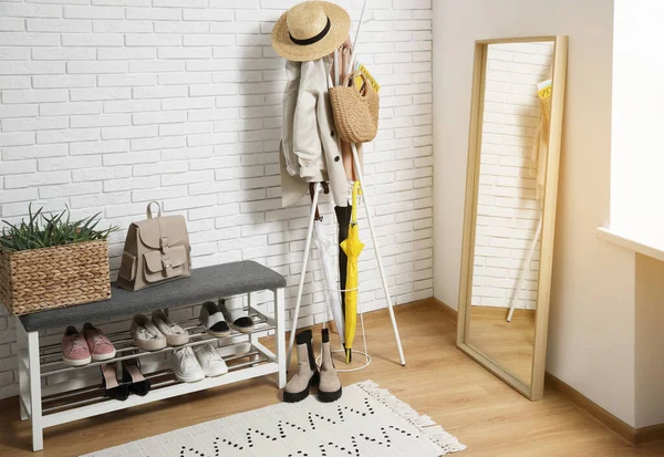 Palto askısı, ayakkabı dolabı ve beyaz tuğla duvarın yanındaki ayna olan şık bir koridor.