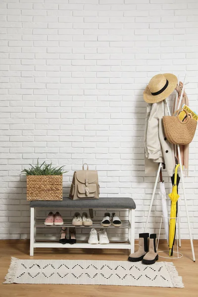 Beyaz tuğla duvarın yanında elbise askısı ve ayakkabı tezgahı olan şık bir koridor.