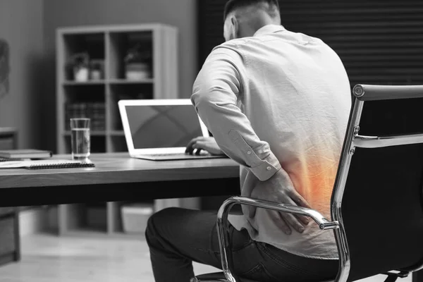 オフィスでノートパソコンを操作しながら腰痛に苦しむ男 姿勢不良の症状 — ストック写真