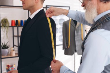 Atölyede ceket kol uzunluğunu ölçen profesyonel bir terzi, yakın plan.