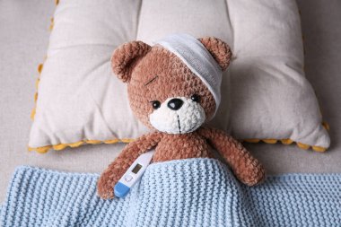 Bandajlı ve yatakta termometresi olan sevimli bir oyuncak ayı. Çocuk Hastanesi