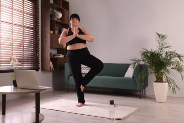 Evde halıda yoga yapan kilolu olgun bir kadın.