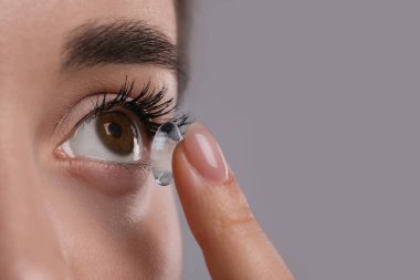 Gri arkaplanla gözüne lens takan genç bir kadının yakın görüntüsü. Metin için boşluk