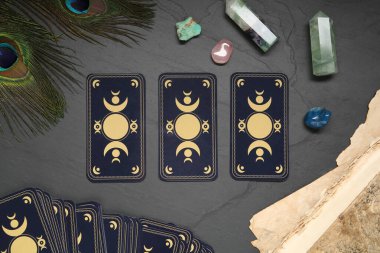 Tarot cards, peacock feathers, gemstones and old book on black table, flat lay. Reverse side clipart