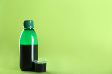 Bir şişe öksürük şurubu ve açık yeşil arka planda ölçü kabı. Metin için boşluk