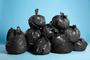 Açık mavi arka planda çöp dolu siyah çöp torbaları