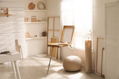 Sanatçının iş yeri ve geniş pencerenin yanında ahşap sehpası olan modern bir stüdyo.