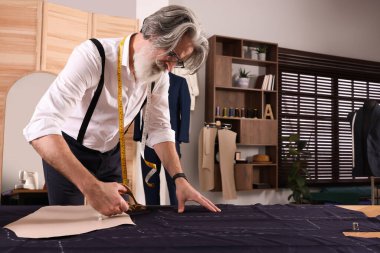 Profesyonel terzi atölyede tebeşirli dikiş kalıbını takip ederek kumaşı kesiyor, metin için yer açıyor.