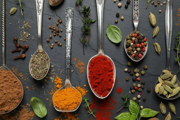 Farklı otlar ve baharatlar, siyah masada kaşıklar, düzlük.