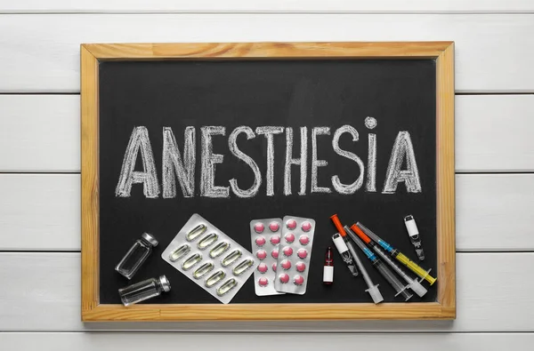 Tahtada kelime anestezi, şırınga ve uyuşturucular beyaz ahşap masa, üst görünüm
