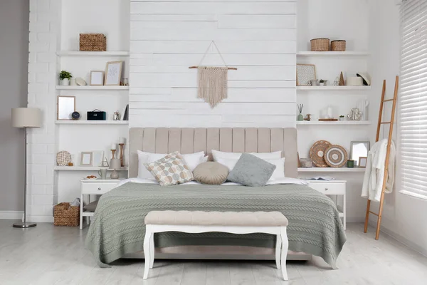 Geniş konforlu yatak, duvar rafları ve güzel dekorasyon elemanları olan şık bir oda.