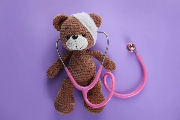 Cute Toy Bear Bandage Stethoscope Violet Background Top View Children — Zdjęcie stockowe