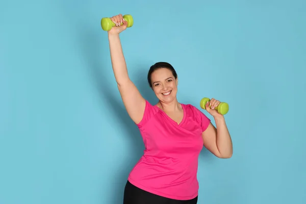 幸せな太りすぎ女性あります演習とともにダンベルオンライトブルー背景 — ストック写真