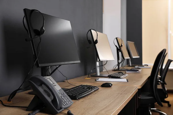 Stationary phone near modern computer with headset on wooden desk in office. Hotline service