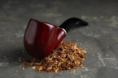 Tütün yığını ve sigara piposu gri masada.