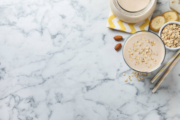 Glass of tasty banana smoothie with oatmeal on white marble table, flat lay. Space for text