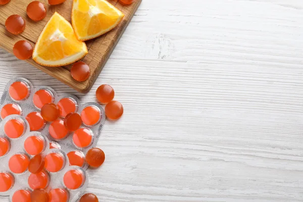 Many orange cough drops on white wooden table, flat lay. Space for text