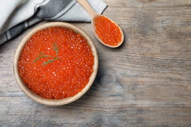 Tahta masa üzerinde lezzetli kırmızı havyarlı kase ve kaşık, düz. Metin için boşluk