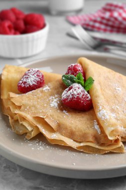 Nane, ahududu ve pudra şekerle servis edilen leziz krepler gri masada, yakın plan.