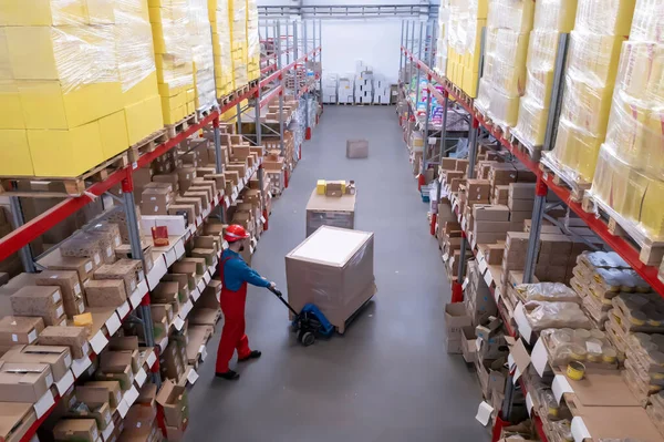 Man in hardhat working with pallet truck at warehouse. Logistics center