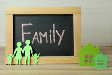 Mutlu Aile Günleri. Tahta, kağıt ebeveynler ve çocukları ahşap masada ev modellerinin yanında.