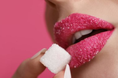 Güzel dudakları olan, pembe arka planda şeker küpü tutan genç bir kadın.