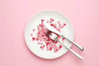 Pembe arka planda kilo verme hapları ve çatal bıçak takımı, üst görünüm.