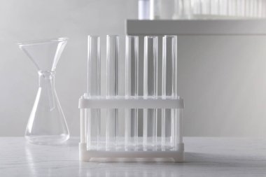 İçerideki beyaz ahşap masada laboratuvar cam takımları var.