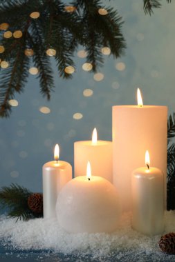 Köknar ağacı dallarıyla mum yakmak, koniler ve mavi ahşap masada yapay kar. Noel atmosferi