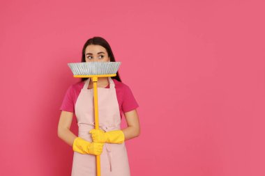 Pembe arka planda süpürgesi olan güzel bir genç kadın. Metin için boşluk