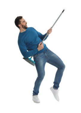 Süpürgeli bir adam beyaz arka planda eğleniyor.
