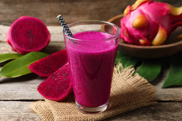 Bir bardak lezzetli pitahaya smoothie ve ahşap masada taze meyveler.