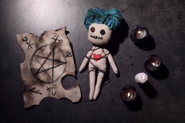 Kalbi iğneli kadın voodoo bebeği ve gri masada tören eşyaları, düz yatıyordu.