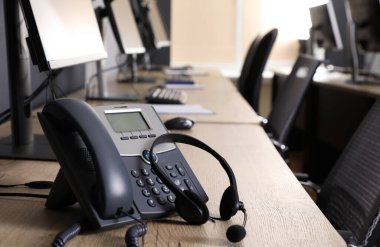 Ofisteki ahşap masada modern bilgisayarın yanında sabit telefon ve kulaklık. Yardım hattı servisi