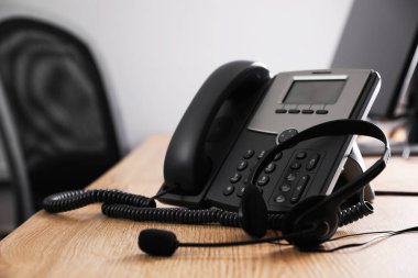 Ofisteki ahşap masada sabit telefon ve kulaklık. Yardım hattı servisi