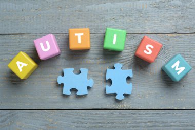 Yapboz parçaları ve gri ahşap arka planda Otizm sözcüğüyle düz kompozisyon