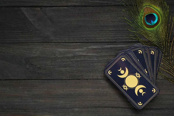 Tarot kartları ve tavus kuşu tüyü siyah ahşap masada, düzlük ve metin için yer var. Ters taraf