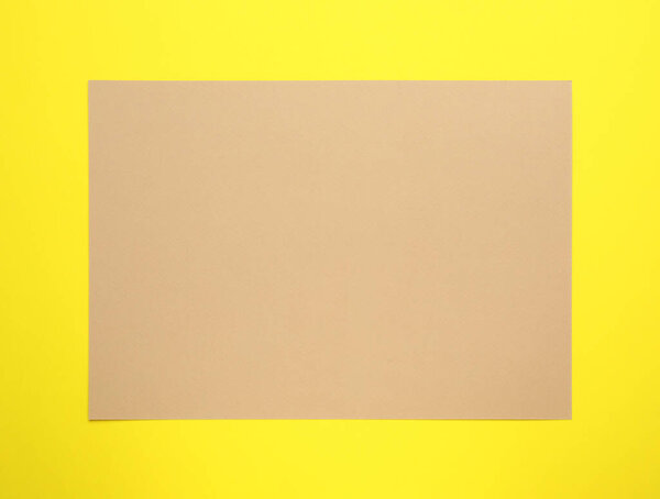 Sheet of brown paper on yellow background, top view