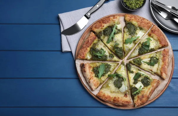 Mavi ahşap masada servis edilen pesto, peynir ve roka ile nefis bir pizza. Metin için boşluk