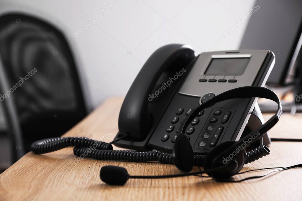 Stationary phone and headset on wooden desk in office. Hotline service