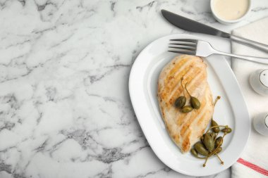 Beyaz mermer masada servis edilen kapari ile nefis pişirilmiş tavuk filetosu. Metin için boşluk