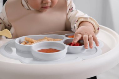 Küçük bebek yüksek sandalyede yemek yiyor, yakın plan.