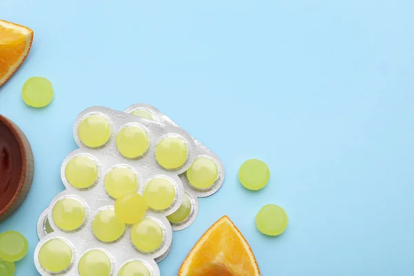 Many cough drops and slices of orange on light blue background, flat lay. Space for text