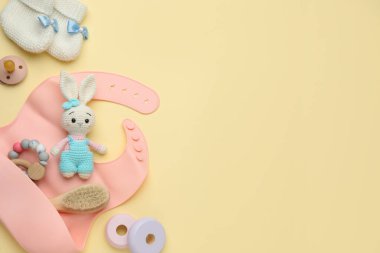 Sarı zemin üzerinde bebek aksesuarları ve önlüğü olan düz kompozisyon, metin için boşluk