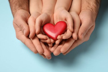 Açık mavi arka planda kırmızı kalbi tutan anne ve baba ve çocuk.
