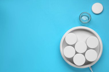 Açık mavi arka planda kavanozları olan modern yoğurt imalatçısı. Metin için boşluk