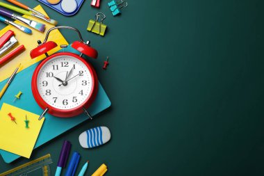 Alarm saati ve yeşil karatahtaya farklı kırtasiye malzemesi olan düz kompozisyon, metin için boşluk. Okul zamanı.